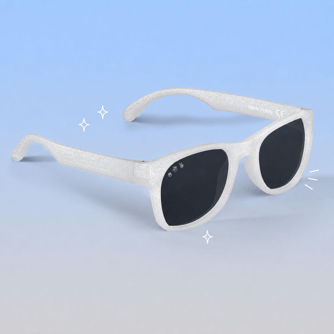 White glittery square sunglasses with dark lenses, shown on a light blue gradient background with small decorative sparkle graphics.